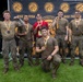A group of six men pose for a photo in front of a 'Bieg Tygrysa' (Tiger Run) event banner in Poland. Most participants are wearing mud-covered military-style camouflage clothing and are displaying finisher medals. The group appears to be celebrating the completion of a military-themed obstacle/mud run event.