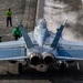 A U.S. Navy carrier-based jet aircraft, marked with the number 510 on both wings, is positioned on an aircraft carrier flight deck preparing for launch. Steam is visible rising from the catapult system in front of the aircraft. Several flight deck crew members in green jerseys and helmets are visible around the aircraft, performing pre-launch duties.