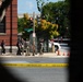 The image shows a law enforcement response scene on Independence Avenue, viewed through tree branches in the foreground. Yellow police tape reading 'POLICE LINE DO NOT CROSS' is stretched across the street, with multiple armed personnel in tactical gear gathered on the sidewalk. Orange traffic cones and a security barrier are visible near what appears to be a secured government facility entrance.