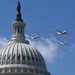 Three U.S. Coast Guard aircraft fly in formation over the dome of the United States Capitol building in Washington, D.C. The aircraft display distinctive white and red Coast Guard livery and appear to be participating in a ceremonial flyover. The Statue of Freedom is visible atop the Capitol dome against a clear blue sky.