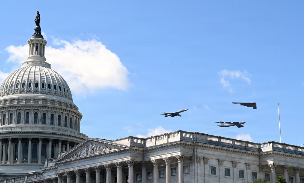 Three U.S. military aircraft are conducting a flyover above the United States Capitol building in Washington, D.C. The formation includes what appear to be a B-1B Lancer, a B-52 Stratofortress, and a B-2 Spirit stealth bomber flying in close proximity. The scene suggests a ceremonial or commemorative flyover event under clear blue skies.