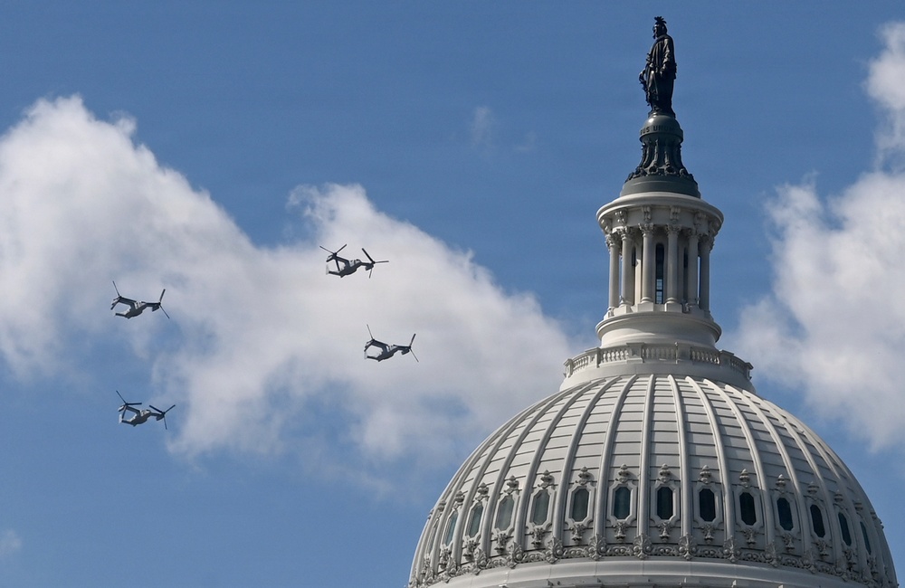Four military tiltrotor aircraft, identifiable as V-22 Ospreys, fly in formation past the dome of the United States Capitol building in Washington, D.C. The Statue of Freedom is clearly visible atop the Capitol dome. This appears to be a ceremonial flyover, likely associated with an inauguration or national event.