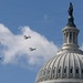 Four military tiltrotor aircraft, identifiable as V-22 Ospreys, fly in formation past the dome of the United States Capitol building in Washington, D.C. The Statue of Freedom is clearly visible atop the Capitol dome. This appears to be a ceremonial flyover, likely associated with an inauguration or national event.