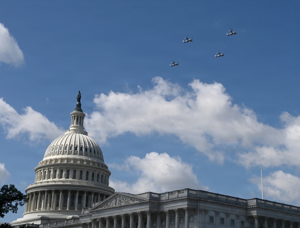 The image shows the United States Capitol Building in Washington, D.C., with its iconic dome and the Statue of Freedom on top. Four military aircraft are flying in formation over the Capitol against a partly cloudy blue sky. The scene appears to capture a ceremonial flyover, likely associated with a national event or commemoration.