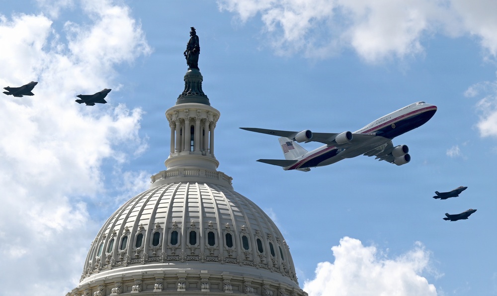 A large military or government Boeing 747-style aircraft with red, white, and blue livery flies over the United States Capitol dome in Washington, D.C. Several smaller military fighter jets are also visible in the sky alongside the large aircraft. The image appears to depict a ceremonial flyover above the Capitol building.