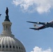 A flyover formation passes above the United States Capitol Building dome in Washington, D.C. The formation includes a large white and red four-engine aircraft bearing U.S. Air Force markings consistent with a VC-25 (Air Force One configuration), accompanied by four smaller fighter jets. The scene appears to be a ceremonial or commemorative aerial flyover.