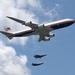 The image shows a large Boeing 747 aircraft bearing the markings 'United States of America' and a Presidential seal, consistent with Air Force One livery, flying in formation with two smaller fighter jets below it. The large aircraft features a white, dark blue, and red color scheme with an American flag on the tail. Two F-35 Lightning II fighter jets appear to be flying in escort formation beneath the larger aircraft against a partly cloudy blue sky.