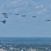 A formation of multiple U.S. military stealth aircraft flying over an urban/suburban landscape under a partly cloudy sky. The formation appears to include a mix of aircraft types including what appears to be a B-2 Spirit stealth bomber, F-22 Raptors, and F-35 Lightning II fighters. This appears to be a ceremonial or demonstration flyover, likely over the Washington D.C. area based on the visible urban landscape.