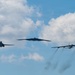 Three distinct US Air Force strategic bomber aircraft are flying in formation against a partly cloudy blue sky. The formation includes all three of the US Air Force's bomber types flying together, a rare and notable display of airpower. The rightmost aircraft is producing visible engine exhaust trails.