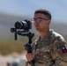 A U.S. Army Sergeant in OCP (Operational Camouflage Pattern) uniform is operating a Sony Alpha mirrorless camera mounted on a DJI gimbal stabilizer in an outdoor desert environment. The soldier appears to be performing official military documentation or media production duties. The patch on the right shoulder suggests a unit or state affiliation.