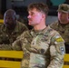 Three U.S. Army soldiers in Operational Camouflage Pattern (OCP) uniforms are seated on yellow benches, appearing to attend a briefing or formation. The central soldier, identified by name tape as 'RASMUSSEN,' wears a Staff Sergeant rank insignia, a '09B' unit patch, a 'Jungle' tab, and an 'A' (Ranger) tab on his left shoulder. The soldiers appear attentive and are in an indoor military facility.