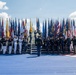 A formal military color guard ceremony is taking place on the National Mall in Washington, D.C., with the U.S. Capitol Building visible in the background. Multiple branches of the U.S. military are represented, with personnel in various dress uniforms carrying a large array of state and military flags. Partial text visible on signage suggests this may be related to a '250th' anniversary or 'Freedom' themed event.