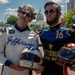 Two individuals dressed as historical U.S. presidents — Thomas Jefferson and Abraham Lincoln — are posing in racing suits at what appears to be a street racing event in Washington D.C., with the U.S. Capitol building visible in the background. Jefferson wears a white suit with number 3 and holds a matching helmet, while Lincoln wears a dark blue suit with number 16 sponsored by 'Gettysburg Energy Drink' and holds a gold-tinted helmet. The scene appears to be a promotional or entertainment appearance at a motorsport event.