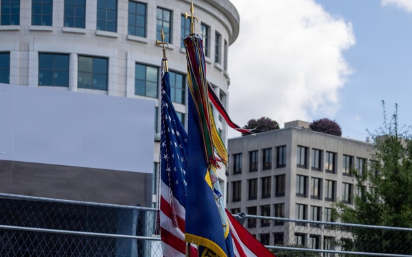 A U.S. Navy color guard is marching in formation carrying flags and rifles at what appears to be the Freedom Grand Prix event. The sailors are dressed in formal white dress uniforms and are performing a ceremonial presentation on a racing circuit. NTT sponsorship banners are prominently displayed along the track barrier in the background.