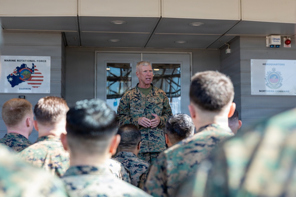 A senior U.S. Marine Corps officer addresses a group of Marines in camouflage uniforms outdoors at what appears to be a military installation. Two signs are visible in the background: one for 'Marine Rotational Force Darwin' featuring Australian and American flag imagery, and another for 'Headquarters Northern Command.' The setting suggests this is a briefing or address at a joint U.S.-Australian military facility in Darwin, Australia.