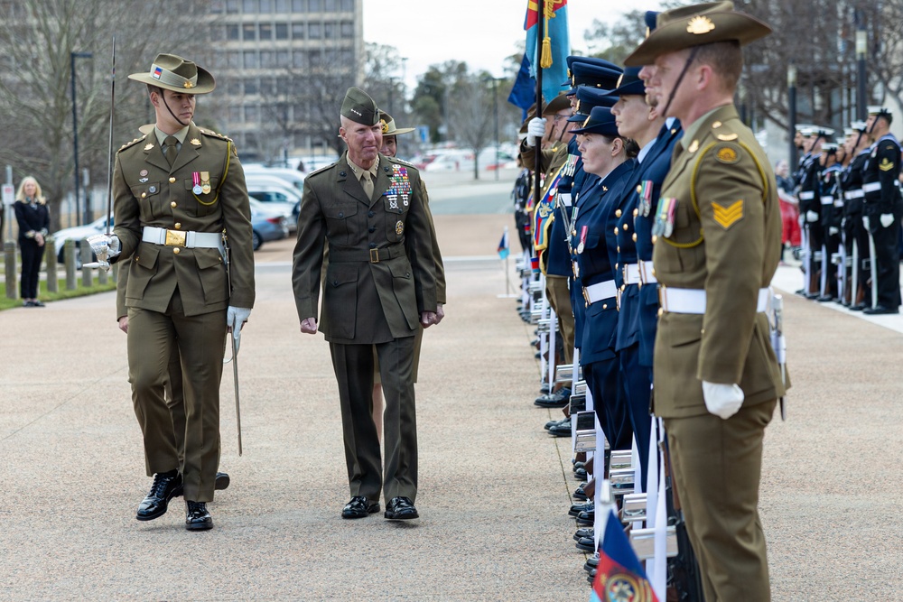 A formal military honor guard inspection ceremony is taking place outdoors, likely in Canberra, Australia. A senior US Marine Corps officer wearing a peaked cap and extensive medal ribbons is being escorted by an Australian Army officer carrying a sword. Personnel from multiple Australian military branches — Army, Air Force, and Navy — are standing at attention in formation.