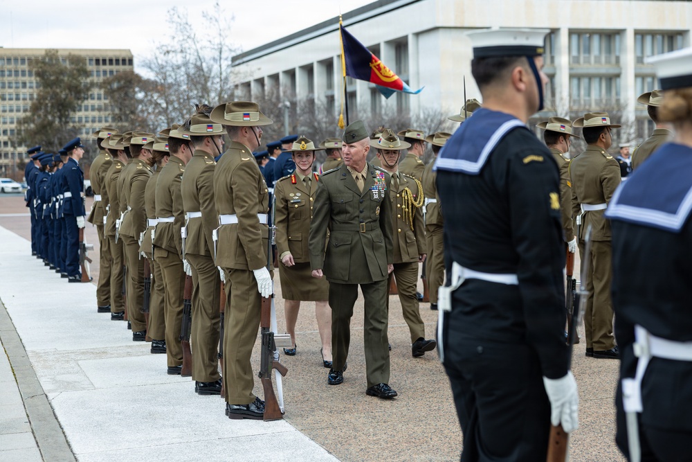 A formal military parade or inspection ceremony is taking place outdoors, likely in Canberra, Australia, based on the distinctive Australian Army slouch hats and the architectural style of the buildings in the background. Two senior officers — one appearing to be a US military officer with a heavily decorated uniform and one an Australian Army officer — are walking along a formed-up honor guard. Multiple branches of the Australian Defence Force are represented, including Army, Navy, and Air Force personnel.