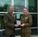 Two senior military officers in dress uniforms are jointly holding a commemorative plaque or award box during what appears to be an official ceremony or exchange. The officer on the left wears a US Marine Corps uniform with extensive medal ribbons, while the officer on the right wears what appears to be an Australian Army uniform with rank insignia and medal ribbons. Both are smiling, suggesting a positive diplomatic or ceremonial occasion.
