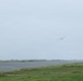A large aircraft is captured in low visibility conditions, appearing to take off or fly at low altitude over what appears to be an airport runway. The scene is shrouded in overcast, hazy weather conditions that significantly reduce image clarity. Green grass borders the paved runway surface in the foreground.