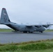 A U.S. Air Force C-130 Hercules military transport aircraft is parked or taxiing on a tarmac apron. The aircraft bears tail code 'YJ' indicating assignment to 5th Air Force, with serial number 838 visible. The rear cargo ramp appears to be open or lowered, and the propellers are spinning, suggesting the engines are running.