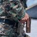 A U.S. Marine in MARPAT woodland digital camouflage uniform is drawing or holstering a pistol at what appears to be a firing range. The name tape 'VARGAS' is clearly visible on the uniform. The Marine is equipped with a tan/coyote brown tactical leg holster mounted on a duty belt.