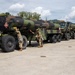Military personnel in camouflage uniforms are working alongside a convoy of large military fuel tanker trucks in a staging area. The tankers are marked with hazardous materials placards (UN 1863) indicating jet fuel (JP-8), and bear 'FLAMMABLE' warnings. The scene appears to be a pre-mission preparation or equipment inspection at a military installation.