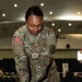 A U.S. Army Sergeant in OCP (Operational Camouflage Pattern) uniform is performing chest compressions on a CPR training mannequin. The soldier, whose name tape partially reads 'ARRO' and wears a Sergeant rank insignia, is demonstrating proper CPR technique in what appears to be an indoor training facility or auditorium. A red-light indicator on the mannequin suggests it is an electronic feedback training device.