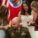 A U.S. Army officer named Parker is seated during what appears to be a military promotion ceremony. Three women, likely family members, are pinning new rank insignia onto his uniform collar and shoulders. The ceremony takes place in front of military flags, including what appears to be the Tennessee state flag and a unit colors flag.