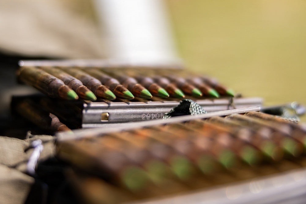 The image shows multiple rifle cartridges with distinctive green-tipped bullets loaded into what appear to be metal stripper clips or magazines. The green tip coloring is a common indicator of armor-piercing or penetrator ammunition. The rounds are arranged in rows on what appears to be a fabric surface.