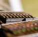 The image shows multiple rifle cartridges with distinctive green-tipped bullets loaded into what appear to be metal stripper clips or magazines. The green tip coloring is a common indicator of armor-piercing or penetrator ammunition. The rounds are arranged in rows on what appears to be a fabric surface.