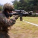 A soldier in camouflage uniform and helmet is aiming a rifle with an optical scope attachment, captured with a radial zoom blur photographic technique that creates a dynamic tunnel-effect composition. The image appears to be taken during a military training exercise in an outdoor field environment. The intentional camera motion blur keeps the weapon barrel as the sharpest focal point of the image.