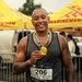 A muscular man with tattoos on both arms is posing proudly after completing a marathon race. He is wearing bib number 206 and displaying a gold finisher's medal around his neck. The event appears to be the 'Run with the Marines' marathon, based on visible text on the bib and background banners.
