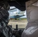 The image is taken from inside a vehicle, looking through the windshield at a parked commercial aircraft on an airport tarmac. The vehicle's seats are covered with black and silver/gray plastic protective covers. At least one ground crew member in a high-visibility vest is visible near the aircraft.