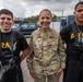 Three military personnel pose together outdoors in what appears to be a military installation or training area. The center figure wears a U.S. Air Force OCP (Operational Camouflage Pattern) uniform with the name tape 'MAYS' and a single star insignia indicating a Brigadier General rank. The two flanking individuals wear black Army PT (Physical Training) shirts and are equipped with what appear to be scuba or breathing apparatus harnesses.