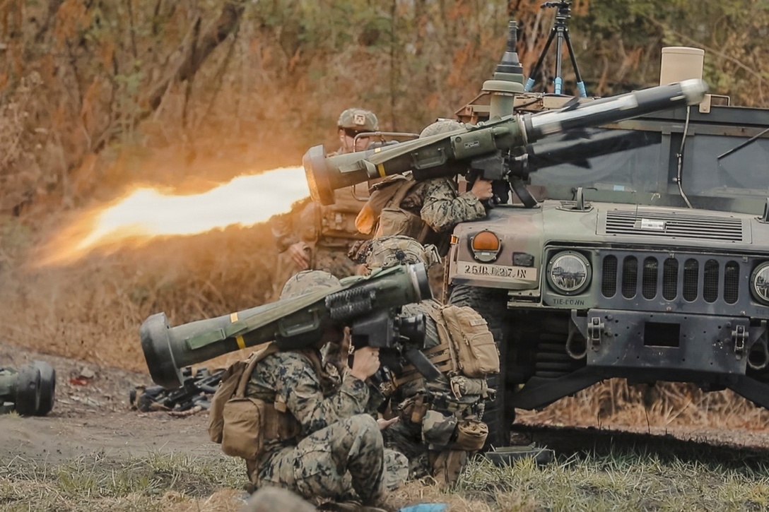 Fire shoots from the back of a shoulder launcher as one of several soldiers behind a vehicle launches a missile in the woods.