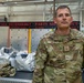 A U.S. Air Force Master Sergeant named Holle is photographed in what appears to be a metals technology maintenance facility. He is wearing OCP (Operational Camouflage Pattern) uniform with visible rank insignia and name tape. The background shows a 'Metals Technology Parts Sign Out' board used for tracking maintenance work orders.