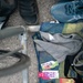 A triathlon or endurance sports transition area setup showing energy nutrition products laid out on a towel next to a bicycle. Multiple energy gel brands are visible alongside cycling/running gear. The scene suggests an athlete preparing for or recovering from a multi-sport event.