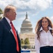 Two individuals are standing outdoors in front of the United States Capitol building in Washington, D.C. The man on the left is wearing a dark navy suit with a red tie, while the woman on the right is wearing a white button-down shirt and dark skirt. The setting appears to be a daytime public event with clear skies and partial cloud cover.