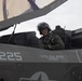 A military pilot is seated in the cockpit of a stealth fighter jet, identified by markings as aircraft number 225, assigned to Lt Col B.M. Boera with the callsign 'Cocker'. The aircraft appears to be an F-35 based on its distinctive stealth design and cockpit configuration. The canopy is open and the pilot is wearing full flight gear including a helmet and oxygen mask connection.