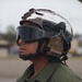 A United States Marine Corps Lance Corporal named Aceret is photographed in profile view on what appears to be a flight line or tarmac. The individual is wearing full flight deck/airfield safety gear including a tactical helmet with communications equipment and protective goggles. The name tape and rank insignia are clearly visible on the olive drab flight suit.