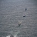 An aerial photograph shows four naval/coast guard vessels sailing in a single-file formation across open ocean. The ships appear to be traveling in the same direction, spaced evenly apart, suggesting a coordinated maritime exercise or transit operation. The lead vessel displays distinctive blue and white hull markings consistent with a coast guard or patrol vessel.