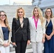 Four women are posing together on the steps of what appears to be a government or institutional building, likely in Washington D.C. based on the neoclassical architecture visible in the background. They are dressed in professional business attire and appear to be at a formal or official event. All four are smiling and facing the camera in a group photo.