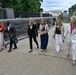 A group of six professionally dressed individuals are walking together along a paved pathway near what appears to be the U.S. Capitol building in Washington, D.C. The group consists of five women and one man, all dressed in business or business-casual attire. The setting suggests an official or formal occasion in a government district.