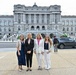 Four women pose for a group photo in front of the Library of Congress Thomas Jefferson Building in Washington, D.C. They are dressed in professional business attire and appear to be visiting or working in the Capitol Hill area. The neoclassical architecture of the landmark building is clearly visible in the background.