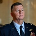 A senior U.S. military officer in dress uniform is photographed in what appears to be an official or governmental building. The individual is wearing a dark blue Air Force-style service dress uniform with multiple decorations and insignia visible. The expression is serious and attentive, suggesting a formal or official occasion.
