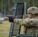 A U.S. Army soldier in full combat gear is firing a pistol at an outdoor shooting range during rainy conditions. The soldier wears a 3rd Infantry Division patch on their helmet and Operational Camouflage Pattern (OCP) uniform with body armor. The image captures an active weapons qualification or training exercise.