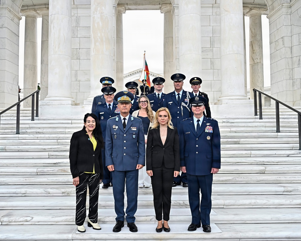 A formal military ceremony photograph taken on the steps of a neoclassical marble building, likely the Memorial Amphitheater at Arlington National Cemetery. The group includes military officers in dress uniforms from what appears to be multiple nations, accompanied by civilian attendees. A flag bearer is visible in the background holding what appears to be a Bulgarian flag.