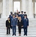 A formal military ceremony photograph taken on the steps of a neoclassical marble building, likely the Memorial Amphitheater at Arlington National Cemetery. The group includes military officers in dress uniforms from what appears to be multiple nations, accompanied by civilian attendees. A flag bearer is visible in the background holding what appears to be a Bulgarian flag.