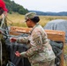 Two U.S. Army soldiers in OCP (Operational Camouflage Pattern) uniforms are working with airdrop equipment in an open field. The female soldier displays an Airborne tab and 173rd Airborne Brigade patch on her left shoulder. They appear to be recovering or inspecting a cargo airdrop bundle with parachute suspension lines after a drop.