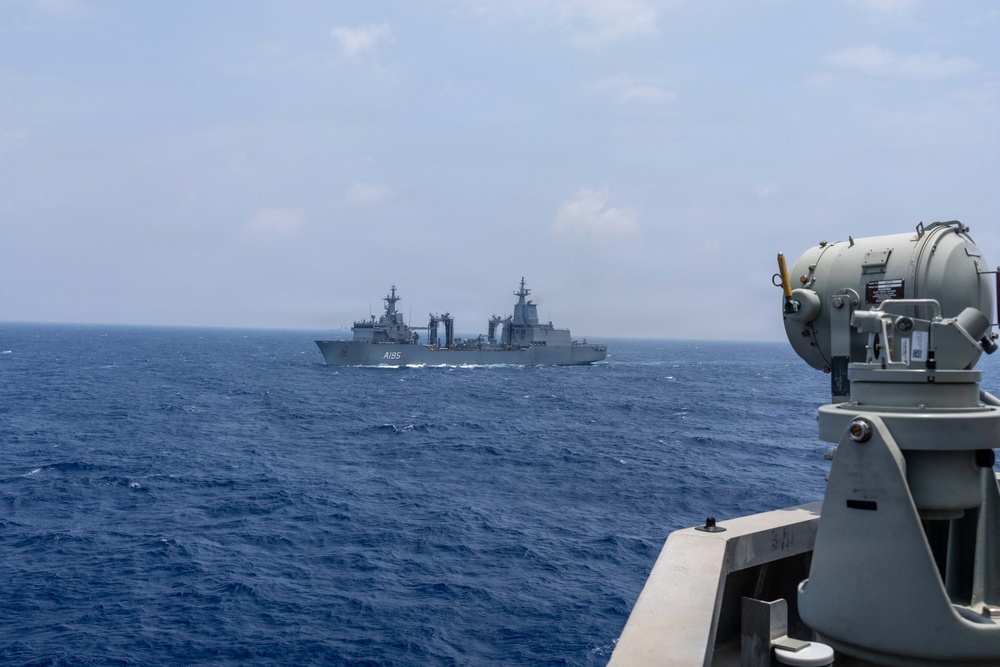 The image shows two naval vessels at sea, photographed from the deck of a third ship. The distant vessel bears the hull number 'A195', identifying it as a naval auxiliary or replenishment ship. A gray optical/fire control sensor system is visible in the foreground on the right side of the frame.